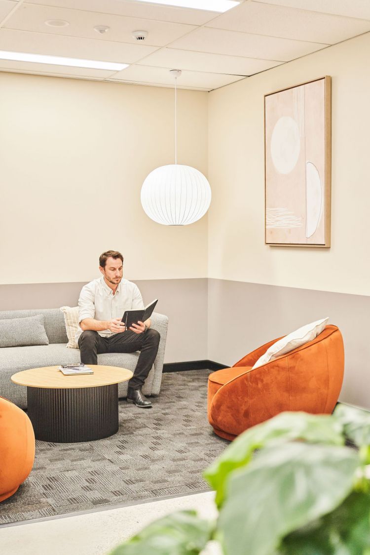 The room features a round wooden coffee table, an orange armchair, a large hanging white spherical lamp, and a framed abstract artwork on the wall